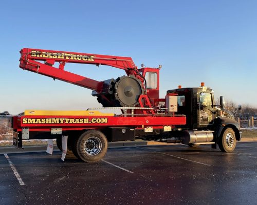 A Smash Truck® from Smash My Trash® parked in an empty parking lot with a blue sky in the background.