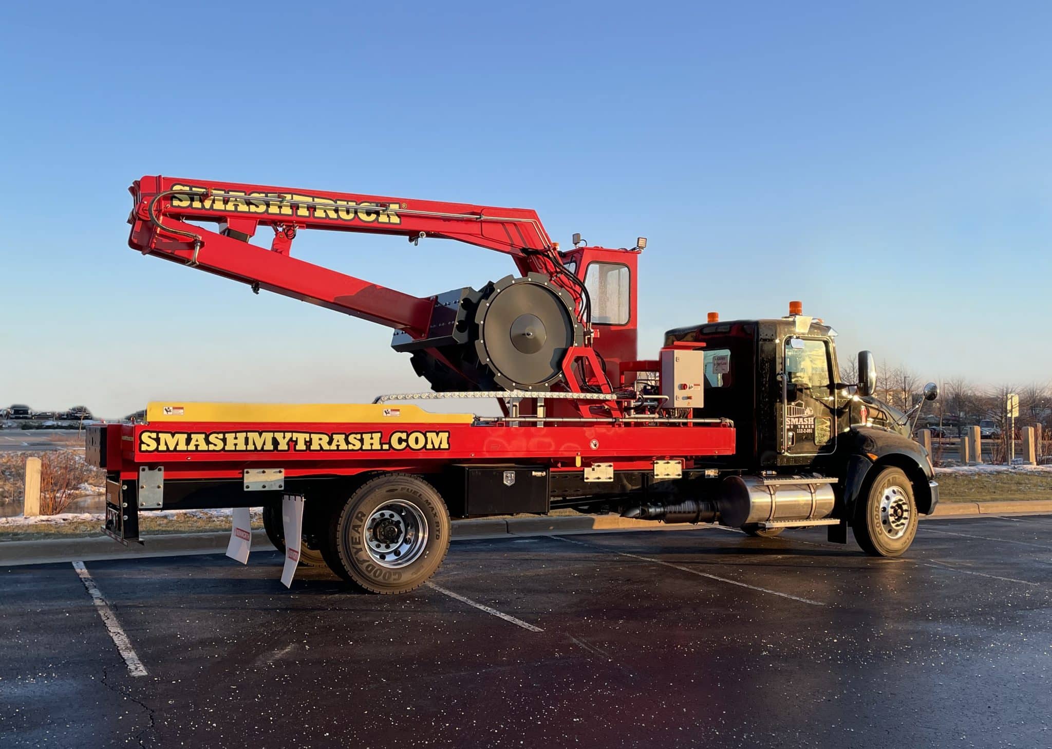 A Smash Truck® from Smash My Trash® parked in an empty parking lot with a blue sky in the background.