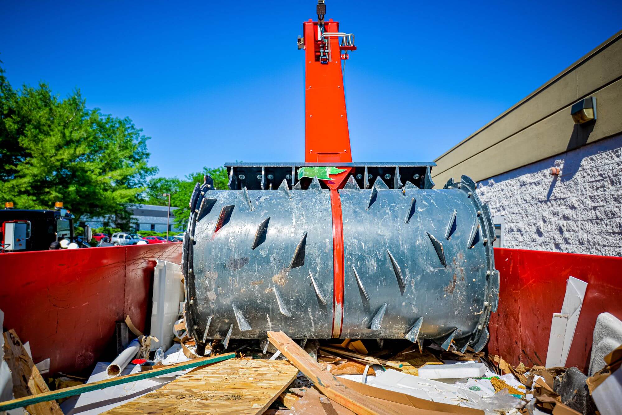 Heavy-duty wood chipper drum inside red dumpster with scattered wood and construction debris